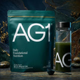 Athletic Greens daily nutrition powder packaging alongside a glass with green nutrient drink and a spoon.